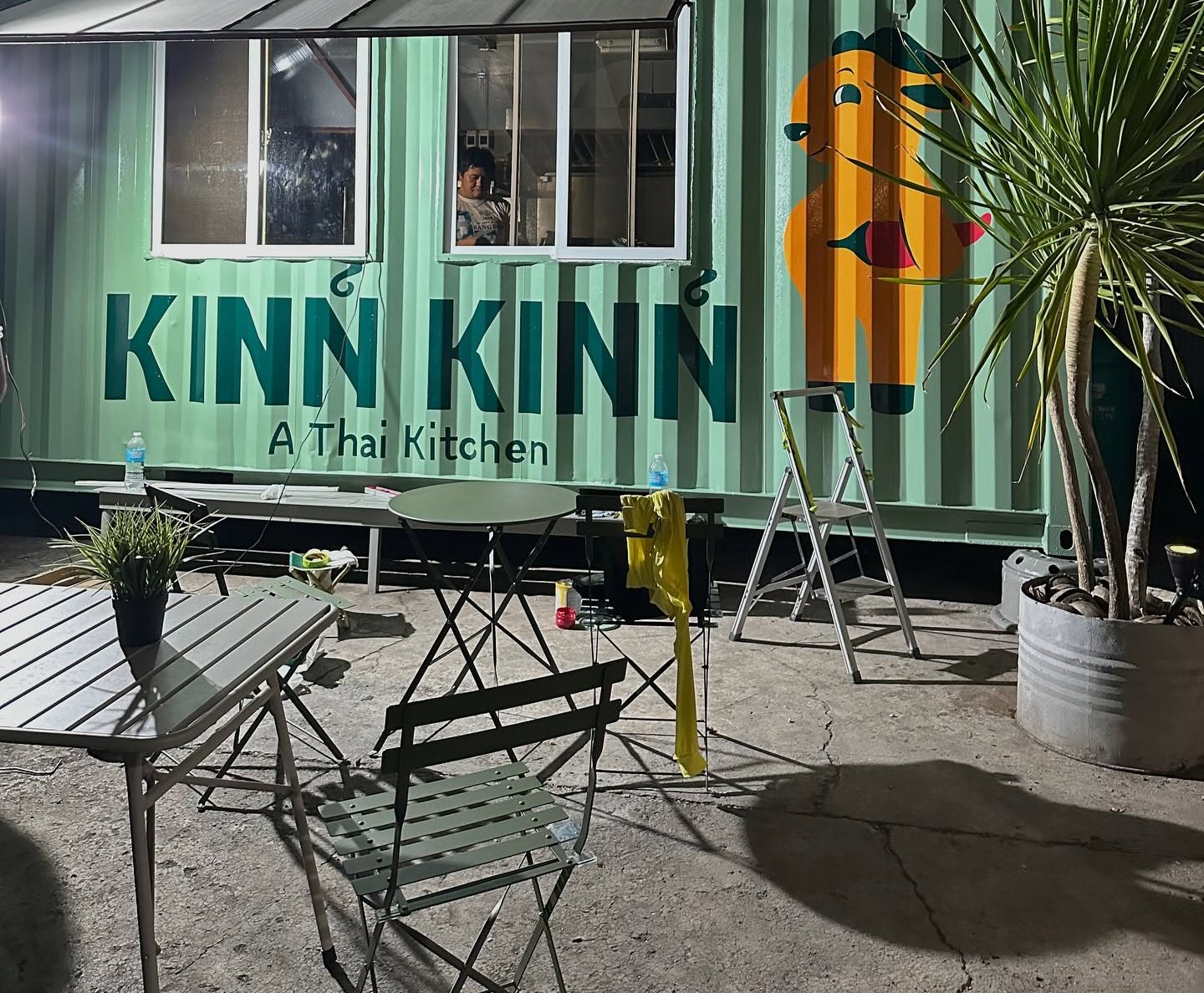 Outdoor tables beside the green Kinn Kinn container, with Buffy the orange water buffalo painted on the wall