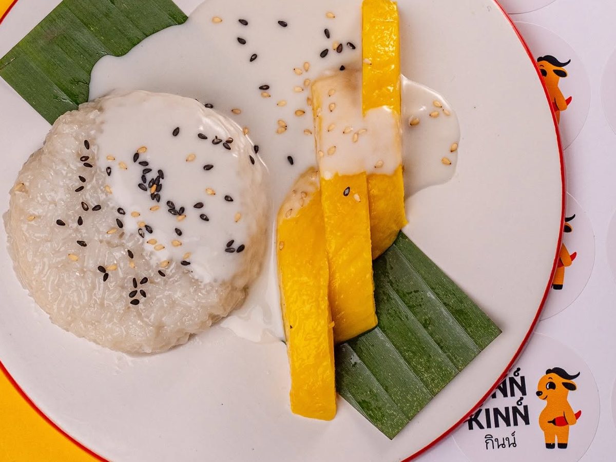 Mango sticky rice on a white plate: sticky rice with coconut cream and sesame seeds, ripe mango and banana leaf